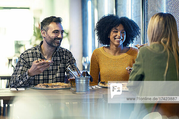 Happy male and female friends enjoying pizza in restaurant