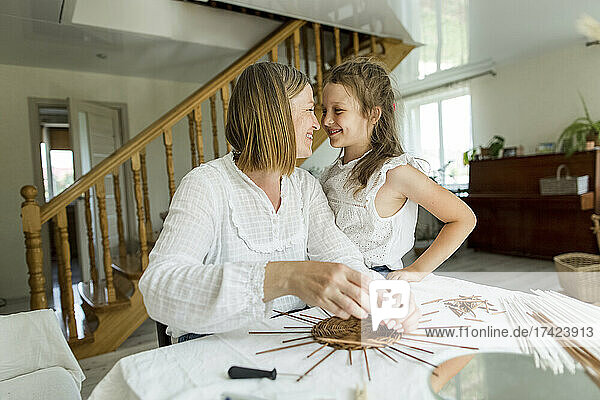 Frau lächelt ihre Tochter an  während sie im Wohnzimmer einen Korb webt