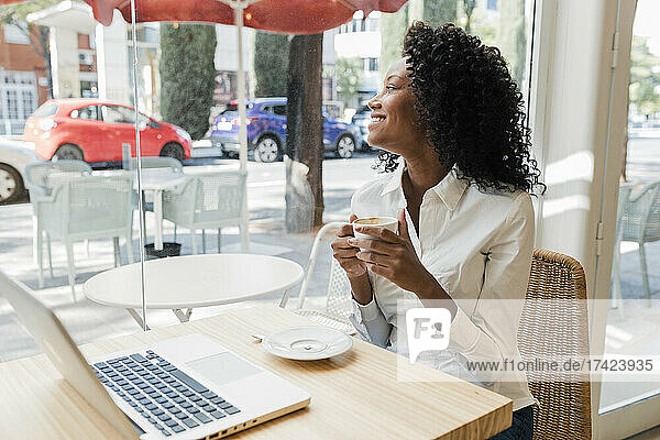 Smiling businesswoman holding coffee cup while looking through cafe window