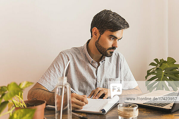 Man looking at laptop while writing in note pad