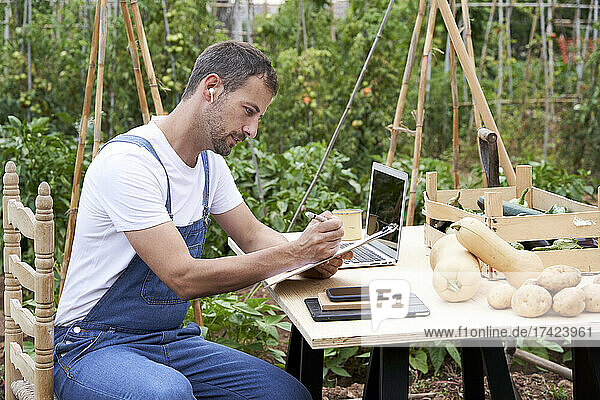 Farmer with clipboard and laptop working at table in farm