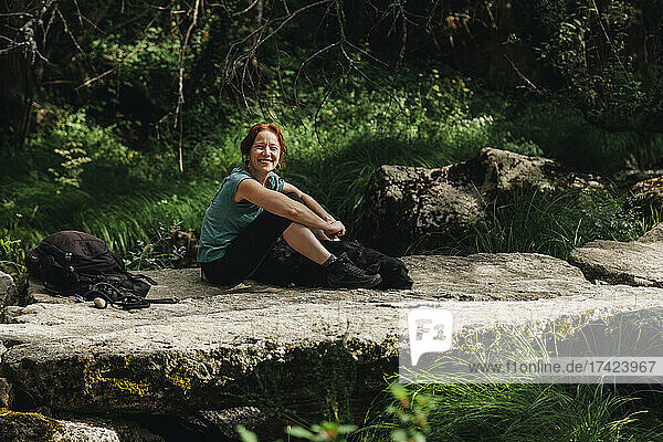 Smiling mid adult woman sitting with dog on footpath in forest