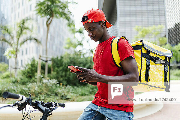 Young delivery man using smart phone while sitting on bicycle