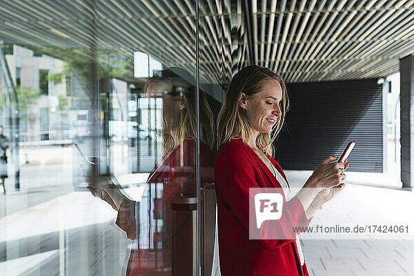 Female professional using mobile phone while leaning on glass wall