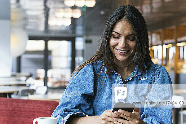 Smiling beautiful businesswoman text messaging through mobile phone while sitting at cafe