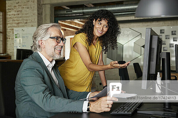 Smiling businesswoman gesturing while discussing over computer with male colleague in office
