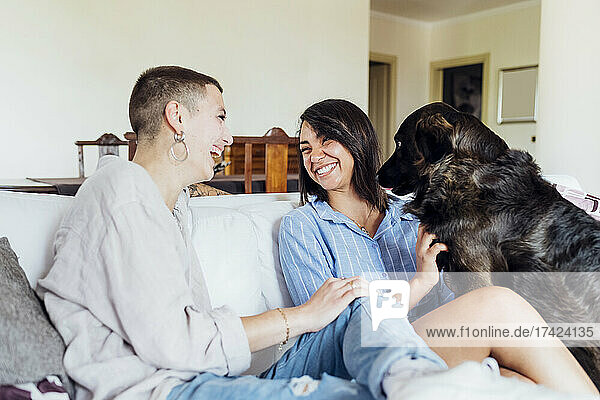 Happy lesbian couple with dog sitting on sofa at home