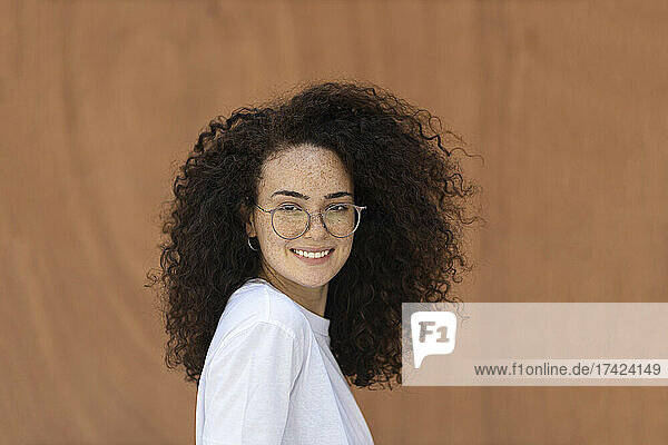 Woman with curly hair in front of brown wall