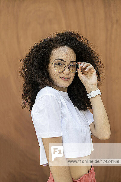 Woman holding eyeglasses in front of brown wall