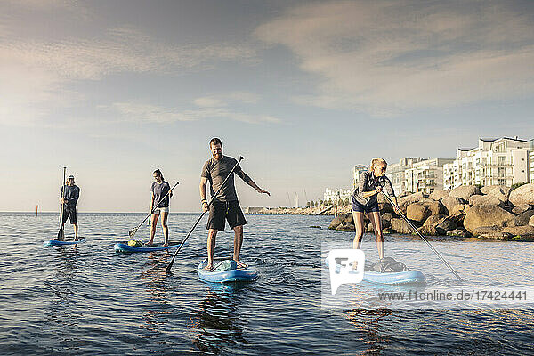 Male and female friends paddleboarding against sky in sea