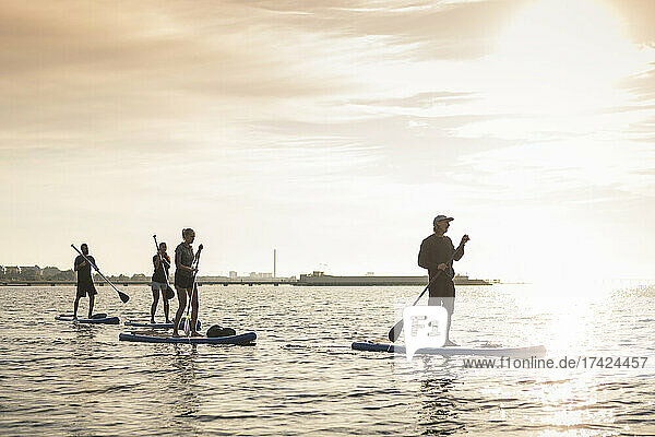 Männliche und weibliche Freunde Paddleboarding im Meer bei Sonnenuntergang