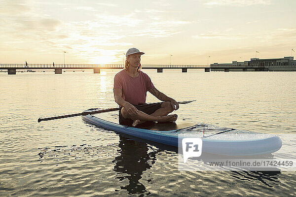 Männlicher Lehrer meditiert auf einem schwimmenden Paddleboard im Meer sitzend