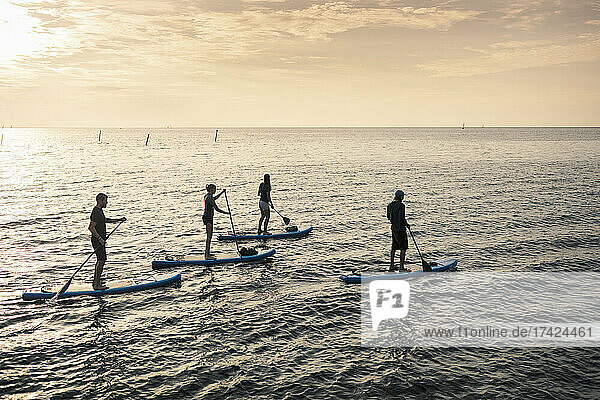 Männer und Frauen paddeln bei Sonnenuntergang auf dem Meer