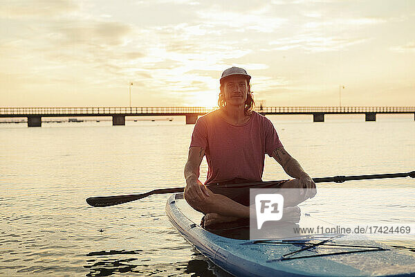 Portrait of man sitting on paddleboard in sea during sunset