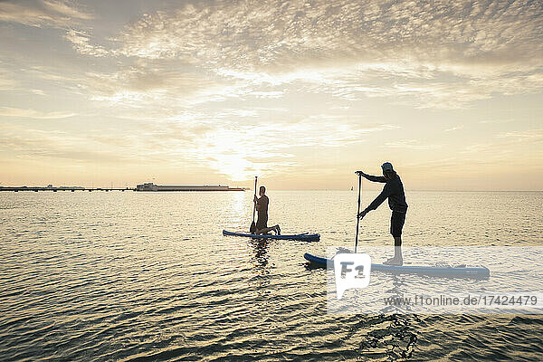 Mann lernt Paddelboard von einem männlichen Lehrer im Meer bei Sonnenuntergang