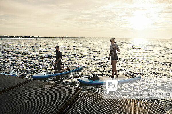 Männliche und weibliche Freunde rudern Paddleboard durch Pier im Meer
