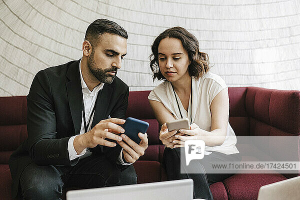 Ein Geschäftsmann zeigt einer jungen Berufstätigen sein Smartphone  während sie zusammen auf einem Sofa im Kongresszentrum sitzen