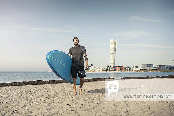 Mann geht mit Stand Up Paddleboard gegen den Himmel am Strand