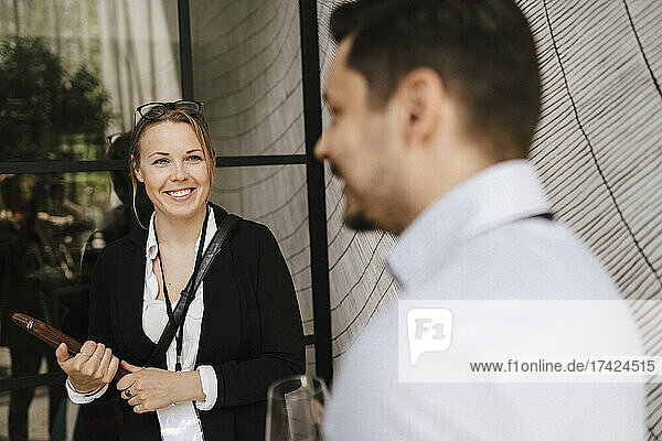 Lächelnde Geschäftsfrau mit Blick auf einen männlichen Unternehmer  der während einer Networking-Veranstaltung im Kongresszentrum diskutiert