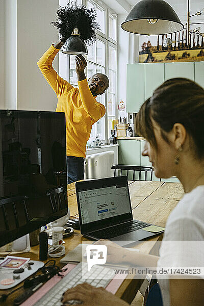 Mid erwachsenen Mann Reinigung Pendelleuchte während weibliche Freiberufler mit Computer arbeiten zu Hause