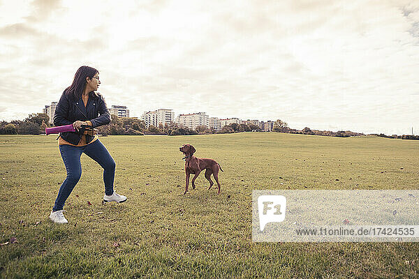 Verspielte junge Frau mit Hund im öffentlichen Park