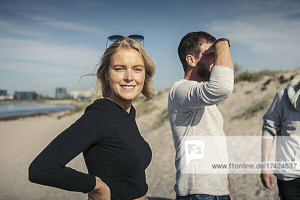 Portrait of smiling woman with male friends at beach on sunny day