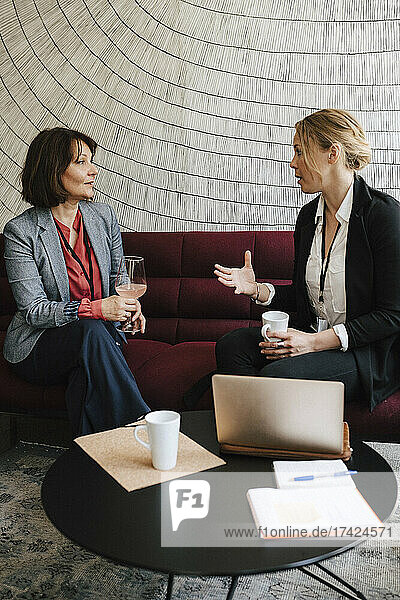Geschäftsfrau gestikuliert  während sie mit einer weiblichen Fachkraft auf einem Sofa im Kongresszentrum diskutiert