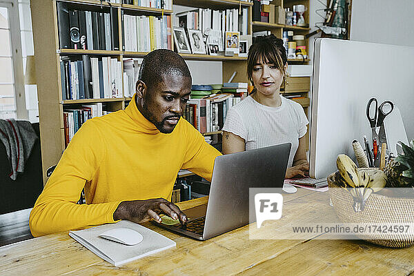 Männlicher Freiberufler mit Laptop  der neben einer Frau am Tisch sitzt