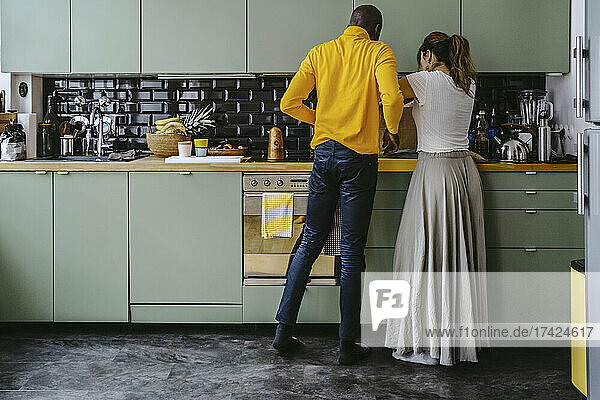 Rückansicht eines Paares in voller Länge bei der gemeinsamen Arbeit in der Küche zu Hause