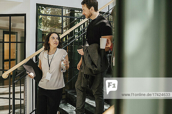 Junge Geschäftsfrau diskutiert mit reifem männlichen Fachmann  während sie auf einer Treppe im Kongresszentrum nach unten geht