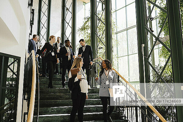 Geschäftsfrau und Geschäftsmann gehen eine Treppe hinunter  während sie im Kongresszentrum miteinander diskutieren