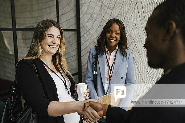 Lächelnde schwangere Geschäftsfrau  die einen männlichen Kollegen begrüßt und ihm während eines Seminars im Kongresszentrum die Hand schüttelt