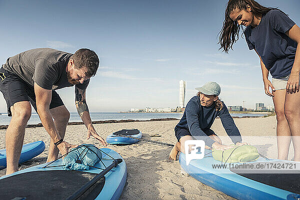 Männliche und weibliche Freunde binden Schlauchboot auf Paddleboard am Strand