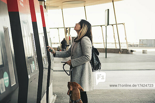Young woman with dog paying through credit card while buying ticket at station