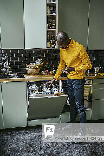 Voller Länge der Mitte erwachsenen Mann tut Gerichte in der Küche zu Hause