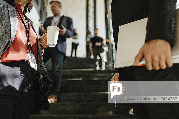 Reife Geschäftsfrau hält Kaffeetasse  während sie mit einem männlichen Kollegen bei einer Networking-Veranstaltung diskutiert