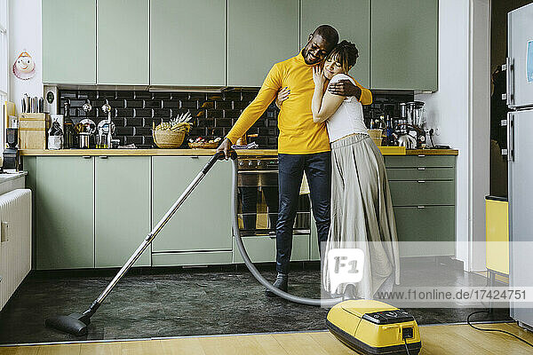 Volle Länge der Mitte erwachsene Frau umarmt Freund mit Staubsauger in der Küche zu Hause