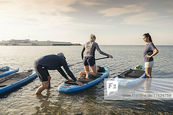 Male instructor teaching paddleboarding to women in sea