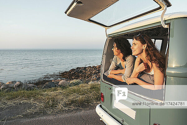 Weibliche und männliche Freunde blicken auf das Meer vom Campingbus aus während einer Autoreise