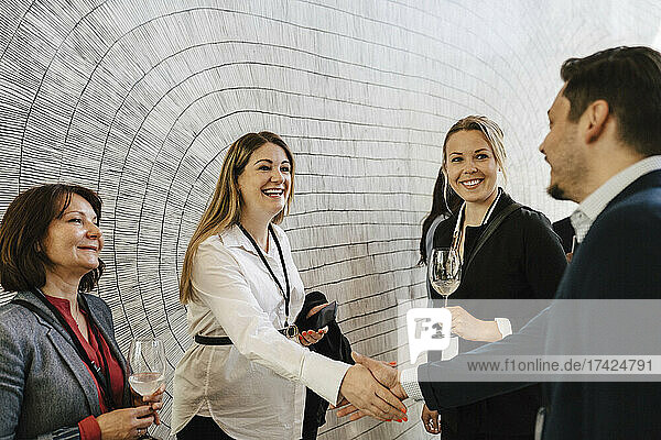 Glückliche schwangere Geschäftsfrau  die einen Geschäftsmann begrüßt  während sie Kollegen im Kongresszentrum die Hand schüttelt