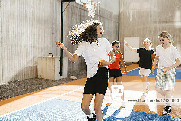 Happy multi-ethnic girls playing in basketball court on sunny day