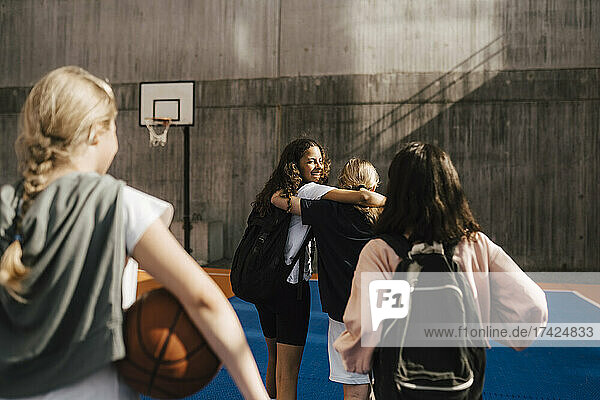 Happy female friends walking with arms around in sports court