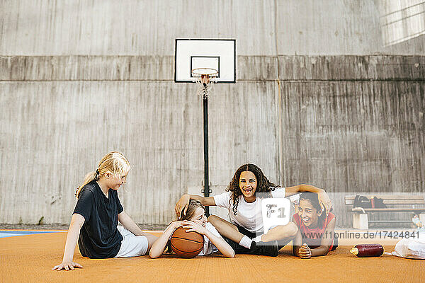 Porträt eines Mädchens  das mit seinen Freundinnen auf dem Basketballplatz sitzt