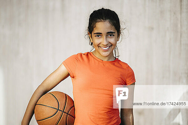 Porträt eines lächelnden Mädchens mit Basketball an der Wand