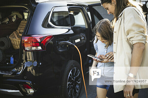 Portrait of mother  father and two daughters standing by car at electric vehicle charging station