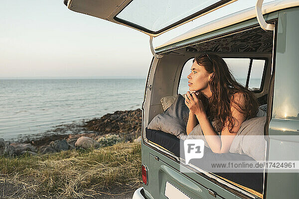 Junge Frau schaut auf das Meer  während sie im Van liegt