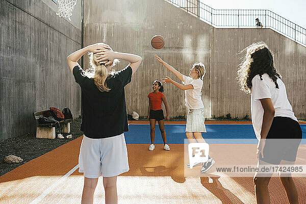 Girl throwing basketball towards hoop while playing with friends at court