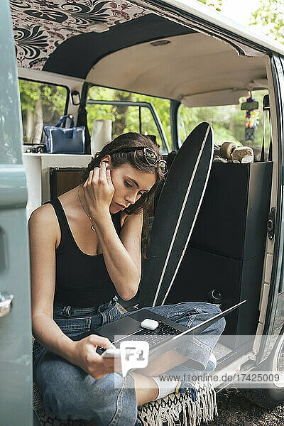 Woman using mobile phone while sitting in camping van