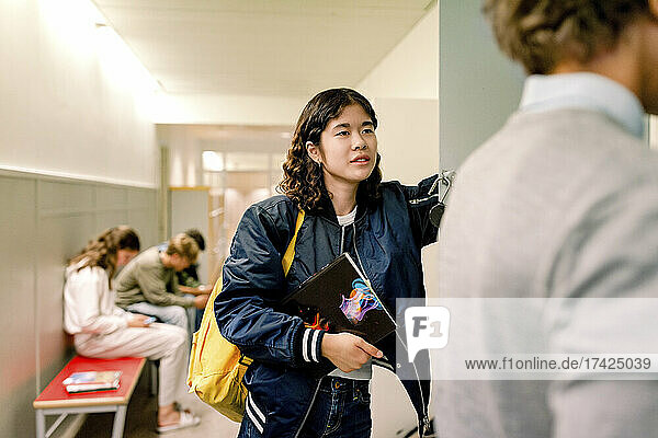 Teenager-Mädchen mit Buch  das einen Jungen in einem Schulkorridor ansieht
