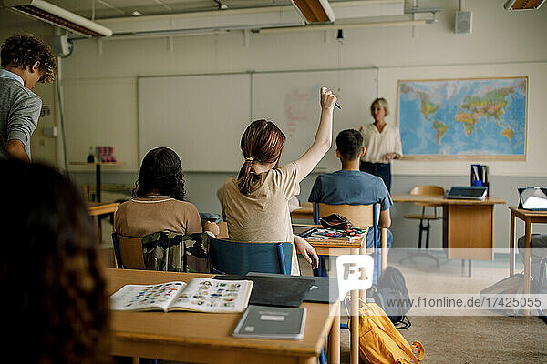 Teenage girl raising hand in high school classroom